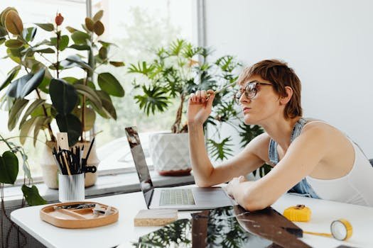pexels-photo-8901137-8901137 Woman in casual wear working on laptop at desk surrounded by plants. Creative and thoughtful workspace.