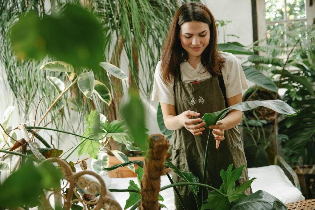 pexels-photo-6231605-6231605 A woman in an apron tending to plants in a lush, sunlit greenhouse.